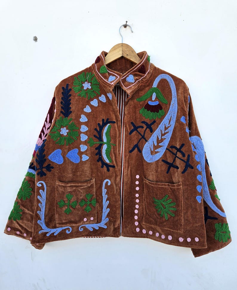 May include: Brown velvet jacket with colourful embroidered floral and paisley designs. The jacket has a collared neckline, two front pockets, and a full-length zip. The embroidery includes shades of blue, green, pink, and white.