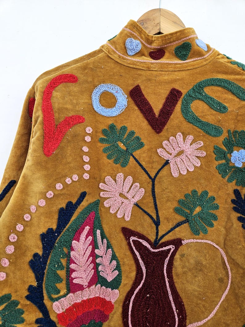 以下が含まれることがあります： マスタード色のジャケット、刺繍入り。 背中には「LOVE」の文字が赤、青、茶色、緑で刺繍されています。 ピンク、緑、青の花柄と葉柄がジャケットを飾り、ボヘミアンな美しさを演出しています。