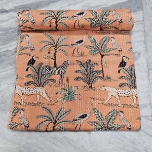 May include: A rolled-up peach-colored quilt with a repeating pattern of zebras, leopards, birds, and palm trees. The quilt is made of a soft material and has a stitched design.