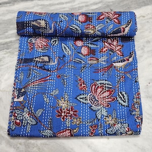 Puede incluir: Un edredón azul enrollado con un diseño floral y de pájaros. El edredón presenta un diseño vibrante con flores rojas, hojas verdes e ilustraciones detalladas de pájaros. Las costuras blancas añaden textura e interés visual a la tela.
