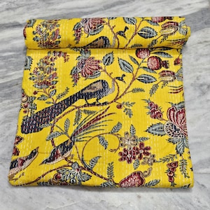 Puede incluir: Un edredón amarillo con un detallado estampado de pájaros y flores. El diseño presenta pavos reales, flores y follaje en tonos de rojo, azul y verde. El edredón está doblado y enrollado, mostrando las intrincadas costuras.