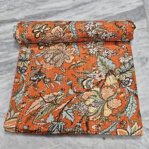 Puede incluir: Un edredón floral naranja con una sección enrollada. El edredón presenta un patrón detallado de flores y hojas en tonos de verde, marrón y crema. Las costuras son visibles, agregando textura al diseño. La estética general es una mezcla de vintage y botánico.