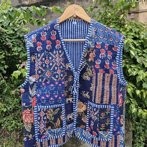 May include: A quilted waistcoat in a patchwork design. The colours are blue, red, and brown. The waistcoat features floral and geometric patterns, and is lined with a striped fabric. It has two pockets and a tie closure.