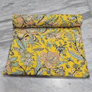 Puede incluir: Un edredón floral amarillo enrollado con un patrón detallado de flores y hojas en tonos melocotón, verde y azul. El edredón está hecho de un material suave y es adecuado para una cama o un sofá.