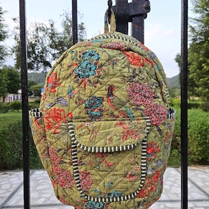 Op de afbeelding: Een gewatteerde rugzak met een bloemenpatroon in groen, rood en blauwgroen. De rugzak heeft een voorvak en zijvakken, met een gestreepte rand. Het ontwerp bevat vogels en bloemen.