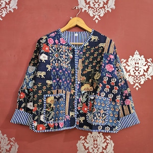 May include: A navy quilted jacket with a patchwork design featuring floral and tiger motifs. The jacket has a round collar, two pockets, and striped cuffs. It is hanging on a wooden hanger.