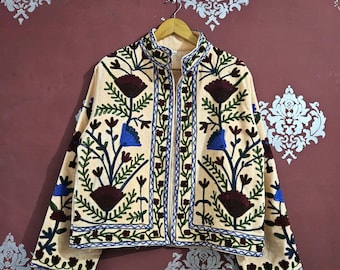 May include: Cream-colored jacket with intricate floral embroidery in shades of burgundy, blue, and green. The jacket features a stand-up collar and is adorned with detailed stitching along the edges and sleeves, creating a bohemian aesthetic.