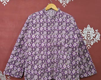 May include: A quilted jacket with a repeating geometric pattern in shades of purple, white, and cream. The jacket is hanging on a wooden hanger against a maroon background. The jacket has long sleeves and a mandarin collar.