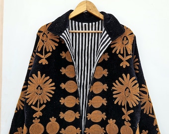 Puede incluir: Chaqueta negra con bordados florales marrones y forro a rayas. La chaqueta tiene un cuello de terciopelo y está colgada de una percha de madera. El bordado presenta grandes diseños de flores y vainas.