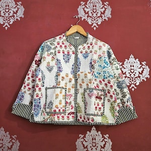 Op de afbeelding: Een wit gewatteerd jack met een bloemen patchwork ontwerp. De jas heeft een opstaande kraag, twee voorzakken en een gestreepte bies. De bloempatronen omvatten rode, blauwe en paarse bloemen.