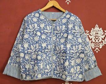 May include: A blue and white floral print jacket with a quilted design. The jacket has a round collar, two pockets, and striped cuffs. It is hanging on a wooden hanger against a red background.