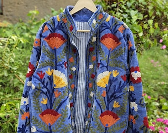 May include: A blue jacket featuring vibrant floral embroidery in shades of orange, yellow, red, and green. The garment has a stand-up collar, long sleeves, and a white and black pinstriped lining visible through the open front closure.