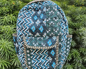May include: A quilted backpack with a geometric pattern in shades of teal, navy, and white. The backpack features a front pocket and a top handle. The design includes a mix of chevron and floral motifs, with brown trim.