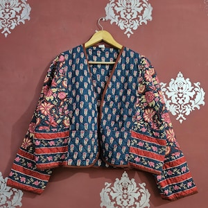 Pode incluir: Casaco acolchoado com fundo azul marinho e padrão floral em rosa e vermelho. O casaco tem decote em V e é adornado com uma borda marrom. As mangas e a bainha inferior apresentam um design listrado vermelho e azul marinho.