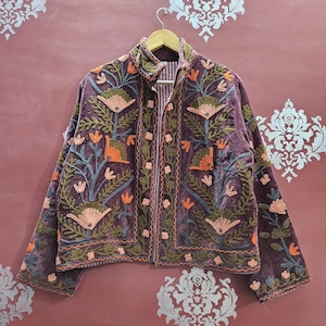 May include: A plum-coloured jacket with detailed floral embroidery in orange, green, and pink. The jacket has a high collar and a zip-up front. The floral design is intricate and covers the front and sleeves.