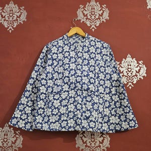 May include: A blue and white floral print jacket with a mandarin collar, hanging on a wooden hanger. The jacket features a repeating pattern of white flowers on a blue background. The jacket is made of a lightweight fabric.