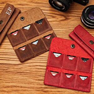 May include: Leather SD card holders in brown and red. Each holder has multiple pockets for storage and a snap closure. The brown holder has the initials "EP" embossed on the front. SD cards are visible in the pockets.