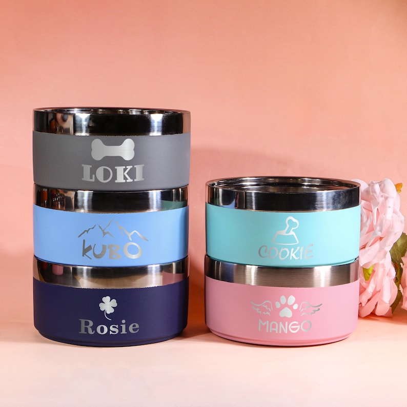 May include: A stack of four stainless steel pet bowls in various colors: gray, light blue, teal, and pink. Each bowl has a silver rim and is personalized with a pet's name and a related icon. The names are Loki, Kuro, Cookie, Rosie, and Mango.