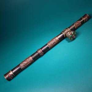 May include: A long, dark pipe with ornate metalwork and decorative accents. The pipe features intricate patterns, red and green gemstones, and a detailed design. The overall aesthetic suggests a vintage or antique style, with a focus on craftsmanship and detail.