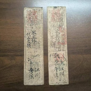 May include: Two antique rectangular wooden blocks with faded black and red ink inscriptions and illustrations. The blocks feature vertical text, symbols, and images of animals. The background is a dark wood surface.