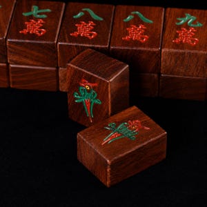 May include: Close-up of wooden Mahjong tiles. The tiles are a rich brown color with red and green symbols. The focus is on two tiles with a detailed bird design. Other tiles with Chinese characters are in the background.