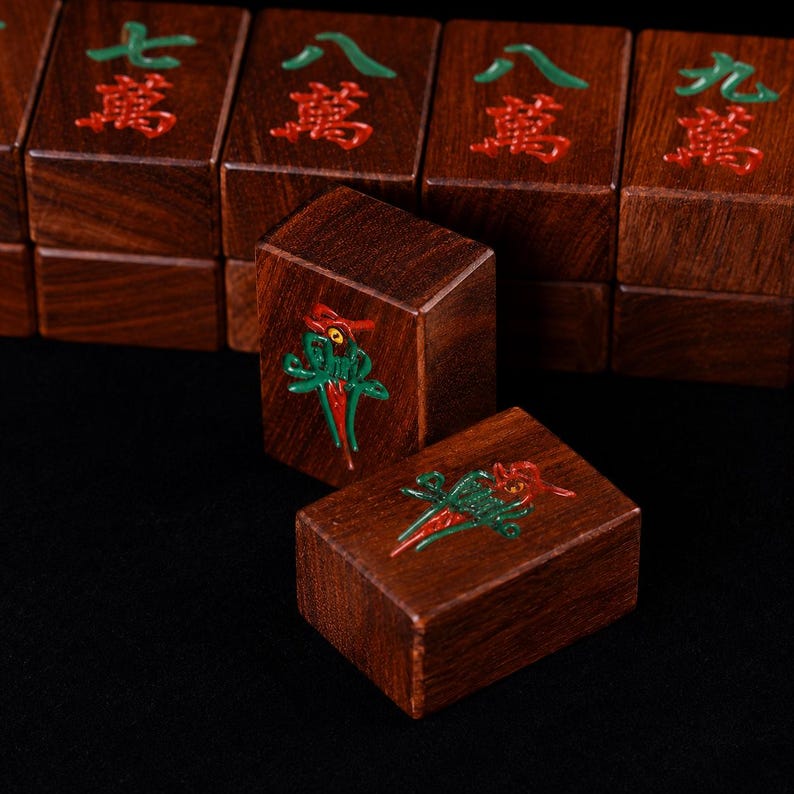 May include: Close-up of wooden Mahjong tiles. The tiles are a rich brown color with red and green symbols. The focus is on two tiles with a detailed bird design. Other tiles with Chinese characters are in the background.