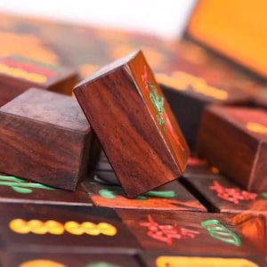 May include: Close-up of wooden Mahjong tiles with intricate carvings and colorful accents. The tiles are a rich brown color, with red, green, and yellow details. The game pieces are arranged on a dark surface, suggesting a game in progress.