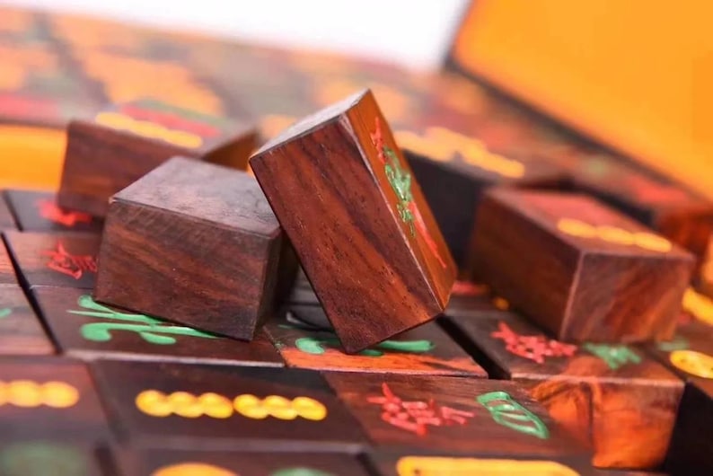 May include: Close-up of wooden Mahjong tiles with intricate carvings and colorful accents. The tiles are a rich brown color, with red, green, and yellow details. The game pieces are arranged on a dark surface, suggesting a game in progress.