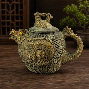 Può includere: Una teiera color bronzo con intricati dettagli di drago. La teiera presenta un beccuccio a forma di testa di drago, un design del corpo del drago e un manico curvo. Il coperchio ha un pomello decorativo. La teiera è appoggiata su una superficie di legno.