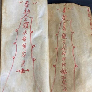 May include: Open book with aged, cream-colored pages. Red calligraphy and decorative lines adorn the pages. The text appears to be in an Asian language. The book is open to two facing pages, with the text and designs visible on both.