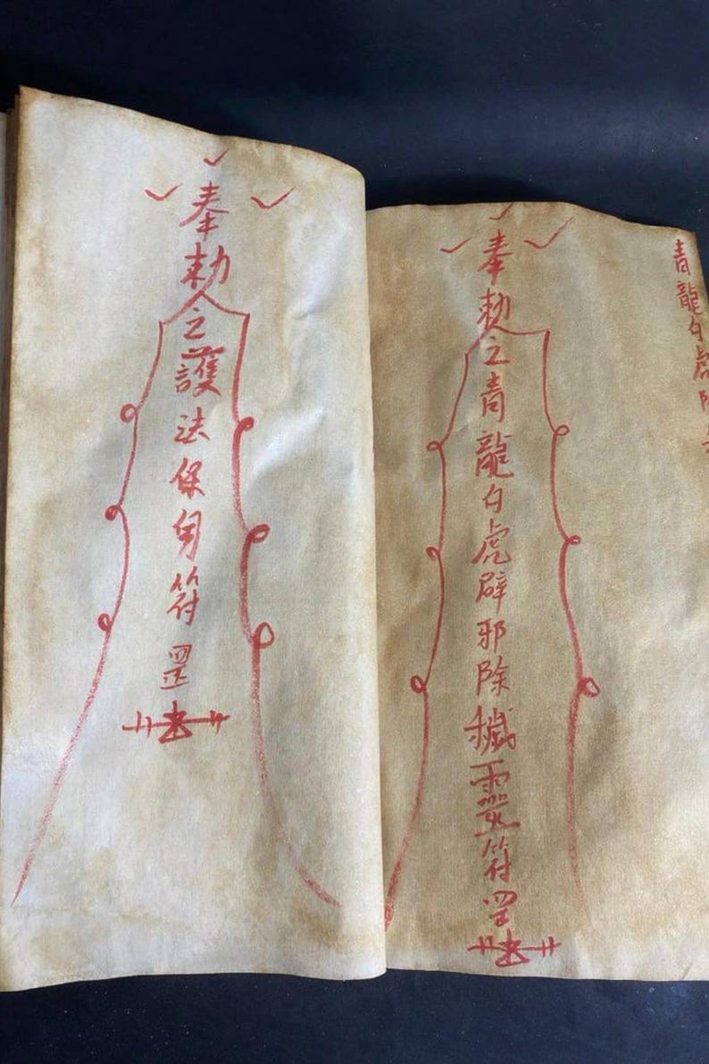 May include: Open book with aged, cream-colored pages. Red calligraphy and decorative lines adorn the pages. The text appears to be in an Asian language. The book is open to two facing pages, with the text and designs visible on both.
