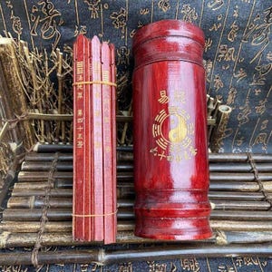 May include: A set of divination tools, including wooden sticks and a cylindrical container. The sticks are bound together with a rubber band and feature vertical text. The container is red with gold Chinese characters and a yin-yang symbol.