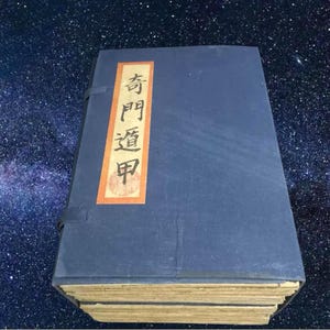 May include: An antique book with a navy blue cover and a rectangular label featuring Chinese characters. The label is orange with black text. The book's pages are aged, and the binding is visible.