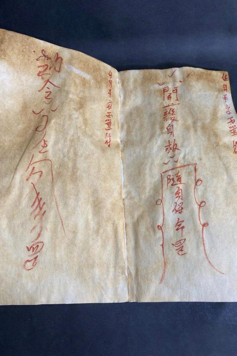 May include: Two-page document with faded, aged paper. Red ink calligraphy and markings cover the pages. The paper has a light brown hue with visible creases. The text appears to be in an Asian language.