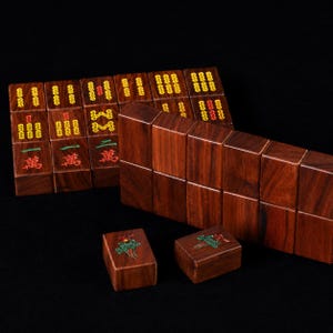 May include: A set of wooden Mahjong tiles with red, green, and yellow markings. The tiles are arranged in stacks and rows, with some displaying Chinese characters and floral designs. The wood has a rich, dark brown color.