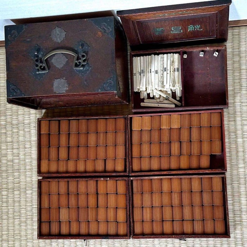 May include: A vintage wooden game set with multiple components. The set includes a large, dark-stained wooden box with metal hardware, several smaller boxes filled with rectangular tiles, and a box containing long, thin game pieces and dice. The game pieces are light-colored.