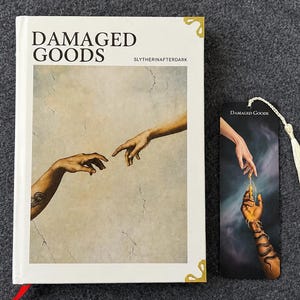 May include: A white book titled "DAMAGED GOODS" with gold corner detailing and a red bookmark. A matching bookmark with a tassel is next to the book. The book and bookmark feature an illustration of two hands reaching out.