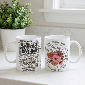 Może przedstawiać: Dwa białe ceramiczne kubki. Jeden kubek zawiera słowa "Positive Vibes" i "Spread Love Hope" z postacią serca. Drugi kubek ma kwiatową grafikę i słowa "You are" z inspirującymi słowami. Oba kubki mają biały uchwyt.