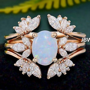 Op de afbeelding: Een roségouden ringenset met een ovale opaal middensteen omringd door marquise-geslepen diamanten. De ring heeft een bloemmotief met meerdere banden. De tekst "JBW" is zichtbaar aan de zijkant.