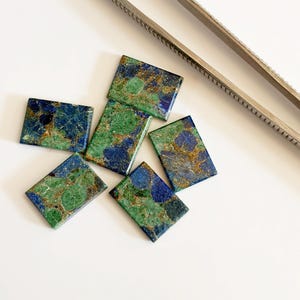 Puede incluir: Cinco cabujones rectangulares de azurita-malaquita con un patrón moteado de azul profundo, verde vibrante e inclusiones doradas metálicas, dispuestos junto a unas pinzas de metal plateado como referencia de escala.