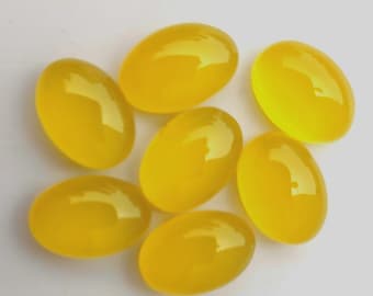 May include: Seven polished, oval-shaped gemstones in a vibrant yellow hue are arranged on a white surface. The stones have a smooth, glossy finish, reflecting light. These gemstones could be used for jewelry making or other crafts.