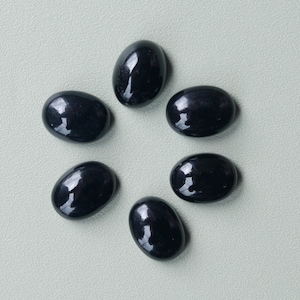 May include: Six polished, oval-shaped black gemstones arranged in a circular pattern. The stones have a glossy, reflective surface, and are set against a light grey background. These gemstones are suitable for jewellery making.