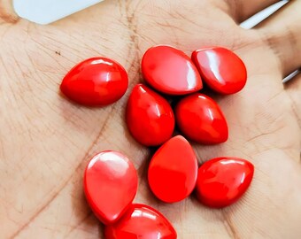 May include: A collection of bright red, teardrop-shaped beads. The beads are smooth and glossy, with a vibrant, solid color. They are displayed in the palm of a hand, showcasing their size and shape.