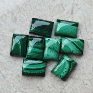 Pode incluir: Uma coleção de pedras de malaquite polidas, cada uma com padrões únicos de redemoinhos em verde escuro e claro. As pedras retangulares estão dispostas sobre uma superfície clara, mostrando sua beleza natural.