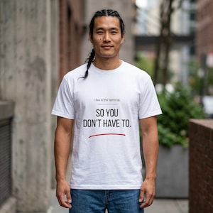 May include: White t-shirt featuring the text "I live in the terminal. SO YOU DON'T HAVE TO." in black, with a red underline. The shirt is worn by a person.