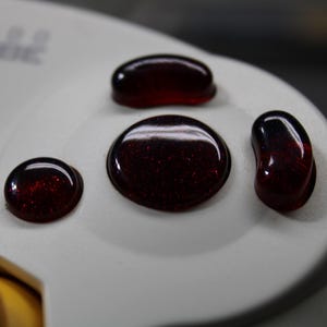 May include: Close-up of a white GameCube controller with several red-tinted buttons. The buttons have a glossy, transparent appearance with a speckled interior. The controller's design is simple and functional.