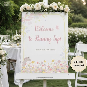 Könnte beinhalten: Ein weißes Schild auf einer Staffelei mit dem Text "Welcome to Bunny Sips". Das Schild ist mit Blumen- und Hasenmotiven verziert und mit weißen Rosen bekrönt. Der Text "Hop On In & Grab a Drink" ist ebenfalls enthalten.