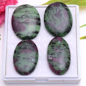Puede incluir: Cuatro cabujones de rubí en zoisita de forma ovalada dispuestos en una bandeja de plástico blanca. Cada piedra presenta una superficie pulida con un patrón moteado de verde bosque profundo, magenta vibrante y pequeñas inclusiones negras.