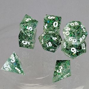 May include: A set of seven polyhedral dice. The dice are clear with green glitter and white numbering. The dice include a four-sided die, two six-sided dice, an eight-sided die, a ten-sided die, a twelve-sided die, and a twenty-sided die.
