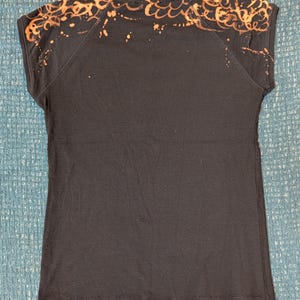 Może przedstawiać: Ciemnoniebieska koszulka z kr&oacute;tkim rękawem. Ramiona i g&oacute;rna część plec&oacute;w mają jasnopomarańczowy wz&oacute;r, ze wzorem rozprysk&oacute;w i fal. Koszulka jest wykonana z miękkiego materiału.